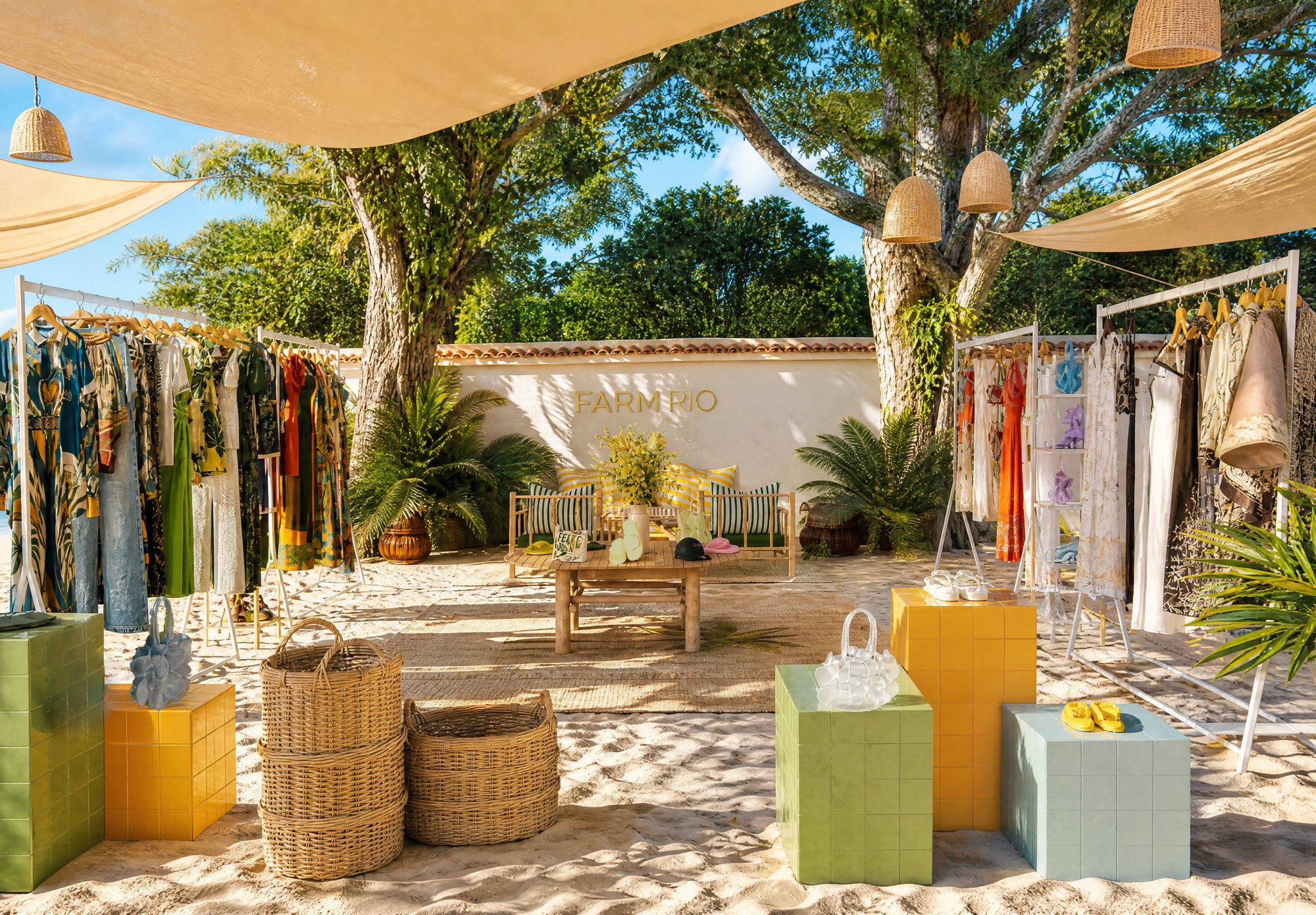 Pop-up ao ar livre com velas de sombra, araras e pedestais coloridos sobre areia